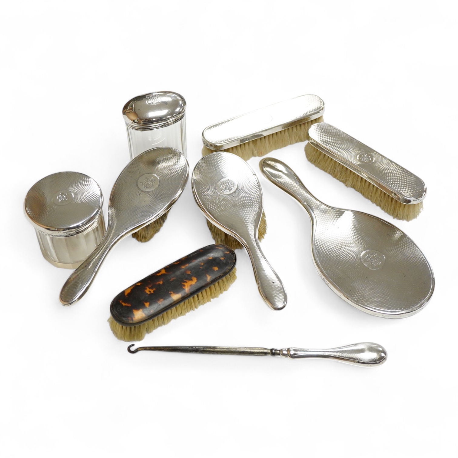A George V seven piece silver mounted toilet set by Charles Henry Dumenil, comprising a hand mirror, four brushes, a glass toilet jar and button hook, London, 1911/12 & 18, together with one other silver mounted toilet j